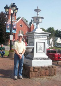 Tony Barry stands next to the refurbished fountain. It stands over nine feet tall and is situated in the Public Square in the center of the village. It is constructed of bronzed iron which is now painted a silver color.  At right, a closeup of the fountain. 