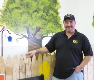 Dave Maynard, Hamlin’s dog control officer, says the dog shelter addition where he is standing was completed in May 2013, doubling the building’s kennels to 20. Volunteers painted trees on the walls for the outdoor effect. Photo by Dianne Hickerson.