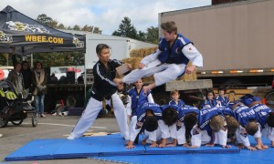 Max Post, 13, a Spencerport resident, uses his foot to break a board held by Master Lim after jumping over seven fellow students lying on the ground. The students of Master Lim Tae Kwondo Academy gave a skillful athletic performance October 5 at the Hilton Apple Fest.