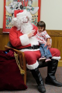 Two-year old Audrey Blake of Clarendon sits on Santa’s lap during Strong West’s Holiday Party. Santa and his elf had a toy and candy for each child attending the event. K. Gabalski photo