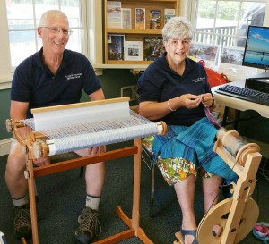 Doug and Cathy Chesnut sometimes weave and spin during their four-hour volunteer shifts at the Welcome Center on the canal. On her small, portable spinning wheel Cathy creates yarn for her knitting and for Doug’s weaving. Doug weaves Japanese “Soari style” on a simple loom. There is no pattern. “You pick your colors and go where you want to go with them,” Doug said.  Doug is color blind, so Cathy spins yarns with colors that are compatible.  On her lap is one of the many stoles that Doug has woven.  Photo by Dianne Hickerson