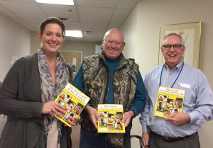 Rhyn McDevitt, Director of Business and Fund Development, and Jim Cummings, Chief Executive Officer, Oak Orchard Health, receive wellness books from Bill Plews, St. Luke’s Episcopal Church. Provided photo