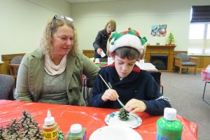 Carole Barrus watches as eight-year old Cash Rosado of Brockport works on decorating a pine cone during the Strong West community holiday party Saturday, December 10 at the Seymour Library in Brockport. K. Gabalski photo