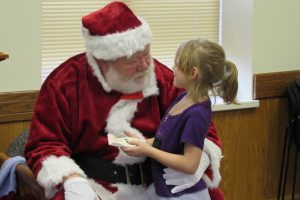 Seven-year old Riley Mayne of Brockport is a captive audience in Santa as she sits on his lap during the annual Strong West community holiday party at Seymour Library in Brockport. K. Gabalski photo