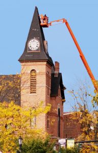 Kyle Didas is at the top of the “135-foot-reach man lift” to repair the church roof and remove the last two hands that were remaining on the clock. Photo by Dianne Hickerson