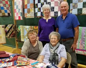 At the Holiday Bazaar, the work of the quilters was on display. Standing are Joan and Jim Smith who cut and sew together the quilt blocks at home.Sitting are Kathy Case (left) and Ruth Stahlecker, two of the quilters who tie the completed tops to the backing material. Started years ago in The Center, the group now works in their new location. Photo by Dianne Hickerson