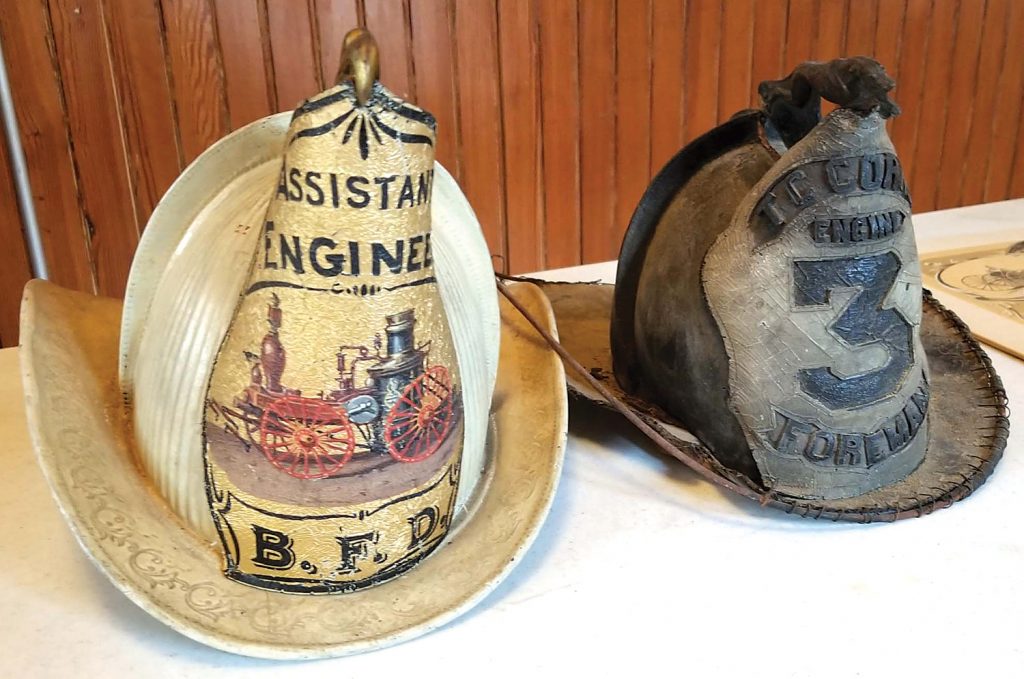 The older helmet (right) reads “T.C. Corn, Engine #3, foreman.” It goes back to the Thomas Corn Engine and Hose Co. that operated the hand pumper. Thomas Corn was a prominent citizen and one of the early presidents of the village. “Foreman” was another word for “Captain.” The newer helmet (left) was worn by the assistant fire chief called an “Assistant Engineer” (word at top) in the late 1800s or early 1900s. Photos by Dianne Hickerson