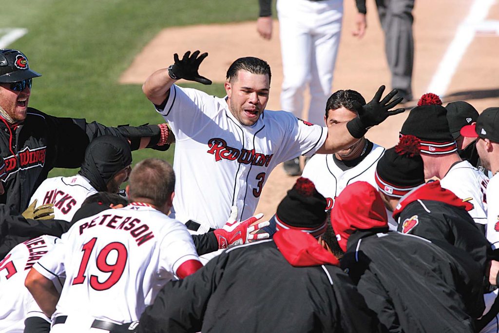 This is a picture of a walk-off home run during the 2015 season. A walk-off home run is described as a home run that ends the game. It must be a home run that gives the home team the lead (and consequently, the win) in the bottom of the final inning of the game. Thus the losing team (the visiting team) must then “walk off” the field immediately afterward. Territo said, “This is the celebration of Josmil Pinto’s walk-off home run at home plate with his team mates. It was during the first game of the season. The Red Wings had 10 walk-off home runs during the 2015 season.”  