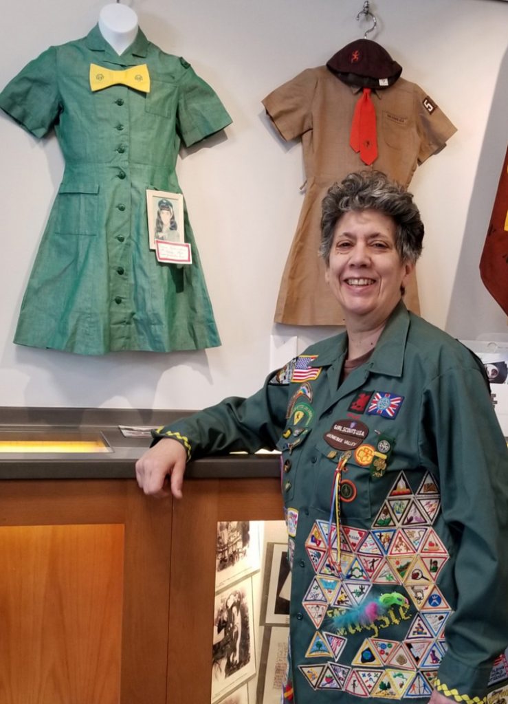Taysie Pennington stands near two uniforms she wore as a Girl Scout. The brown one was for her Brownie Girl Scout membership in 1966. The next year she moved up to Intermediate Girl Scout (the name then) and wore the green uniform. The photo attached for display shows her wearing it in fifth grade. Her jacket she is wearing displays a wide variety of Scout badges and pins. Photo by Dianne Hickerson