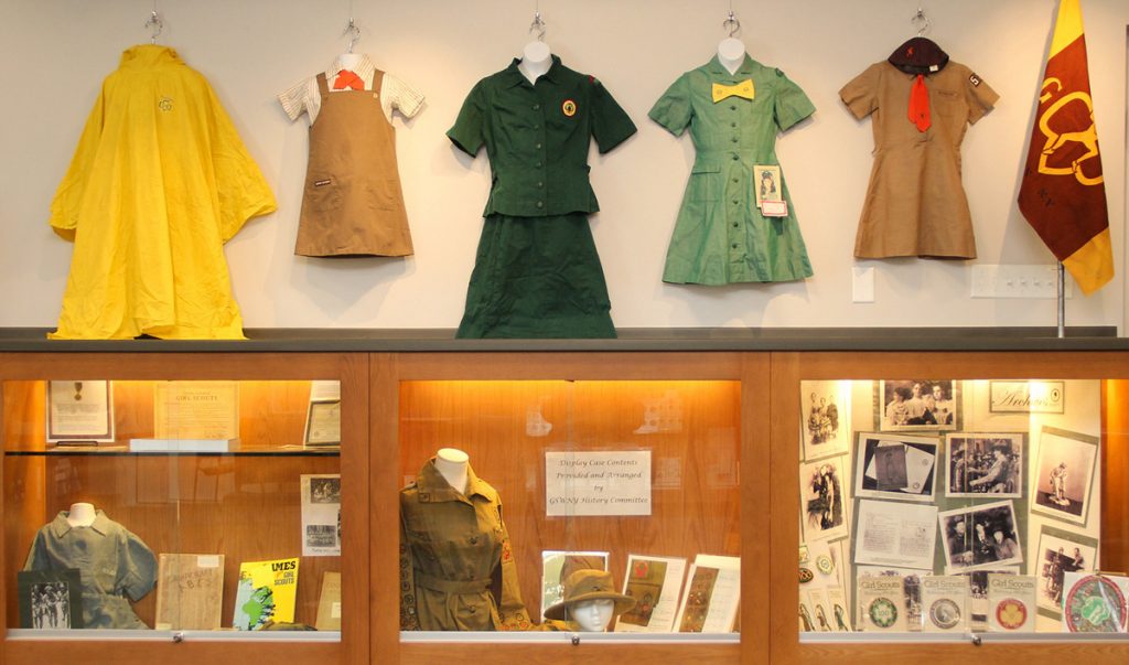 One wall in the Local History Room shows uniforms provided by Taysie Pennington. The two on the right belong to Taysie and are explained in another photo. The yellow raincoat is Taysie’s, used in summer camp. The next is a Brownie uniform. The green one is a Senior Scout uniform, both obtained at VOA and their dates are unknown. The central display case contains the 1919 first Scout uniform, sash and merit badges. Photo by David Q. McDowell