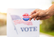 Hand showing I voted today badge at ballot box at american elections.